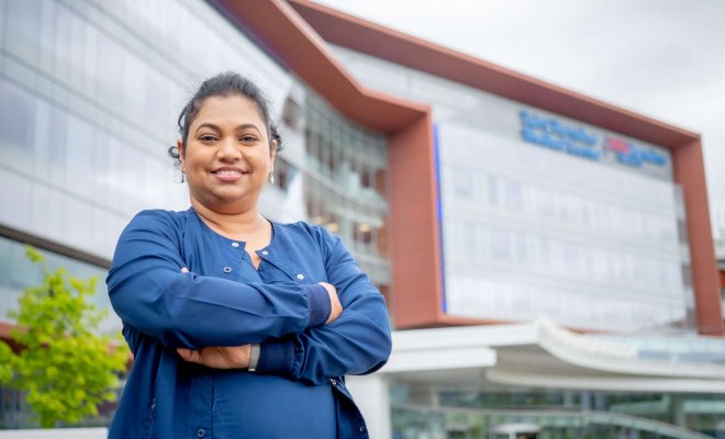 Nursing alumna Sandy Hussain in scrubs standing in front of hospital