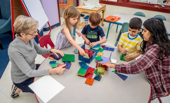 Teachers working with very young students at a low table on a class project involving colorful magnetic blocks.