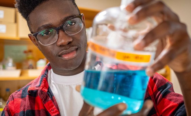 A student in a lab holding a glass flask holding a blue liquid