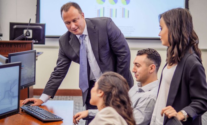 Professor and students talking while looking at a computer screen.