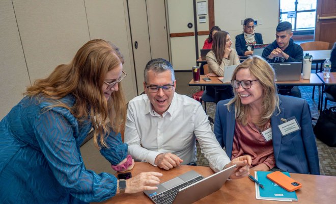 A university professor shows adult learners an assignment on a laptop in a classroom setting.