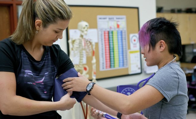 One student takes another student's blood pressure in a classroom.