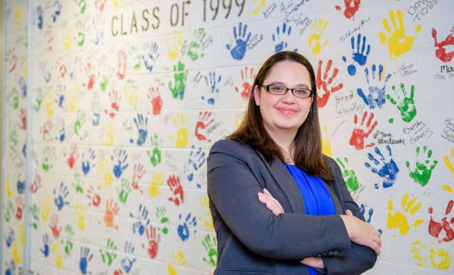 An educational administrator poses in front of a decorated school wall.