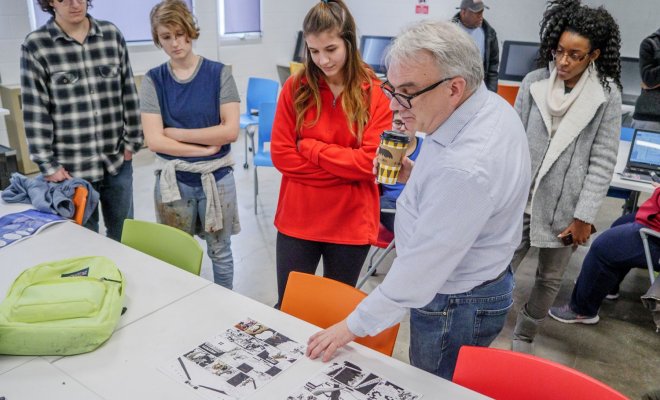 A teacher evaluates at an assignment as a group of students look on.