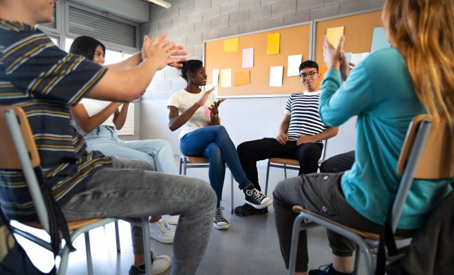 Young people in a community center sit in a circle, applauding one member for sharing.