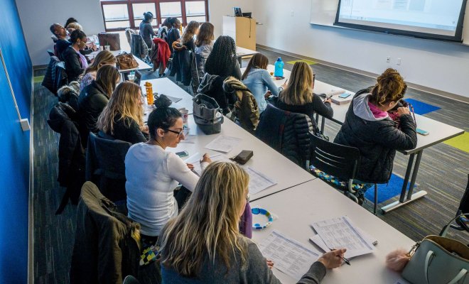 Students at tables in two rows in a brightly lit classroom