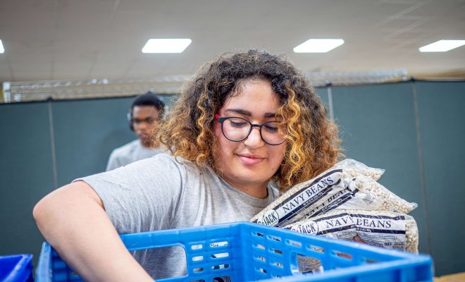 A student volunteer packs bags of navy beans into a crate.