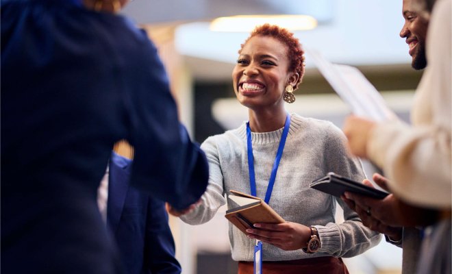 A woman in business-casual clothes wearing a lanyard shakes hands with someone off-camera