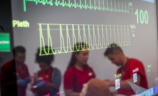 Medical machine with yellow and green streaks, through the reflection there are nursing students in scrubs.