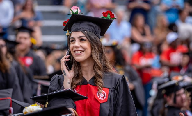 Graduate at commencement on her phone smiling.