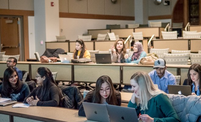 Auditorium full of students on their laptops discussing material.