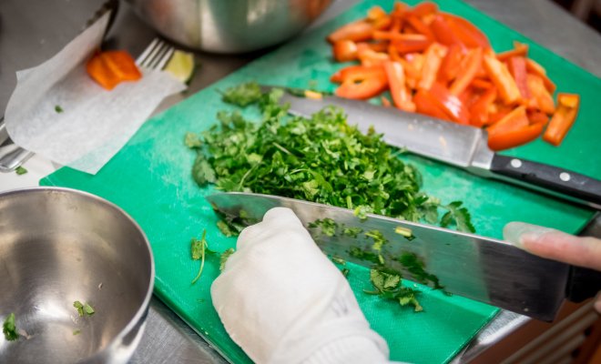 Someone is using a knife to cut cilantro on a green cutting board next to cut up peppers.