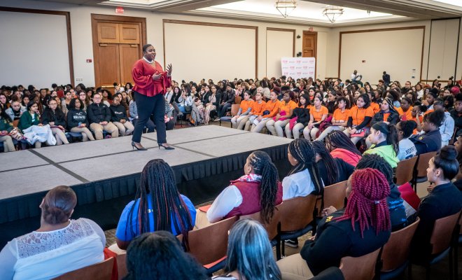 Female on stage is speaking to auditorium full of students.