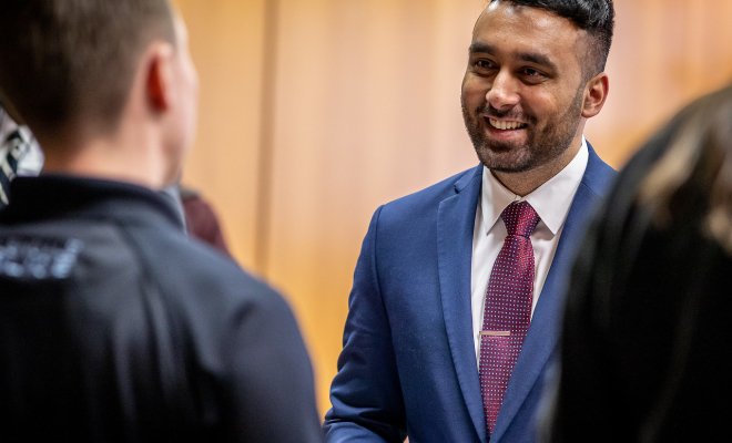 Man in a suit at a career fair speaking with another individual.