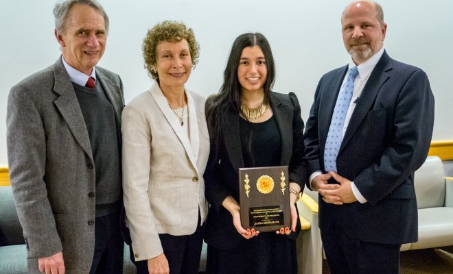 Student is holding an award next to professors aside her while she is smiling.