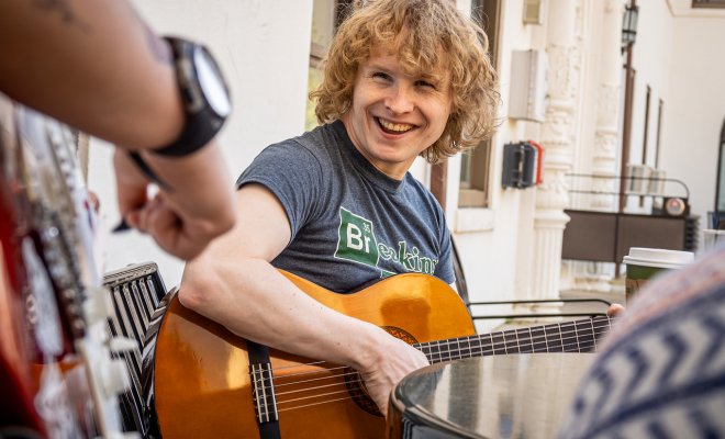 Student smiling while playing guitar wearing a breaking bad tshirt.