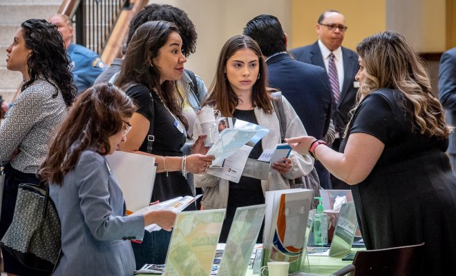 Three females are at a table listening closely to another woman explaining something to them.