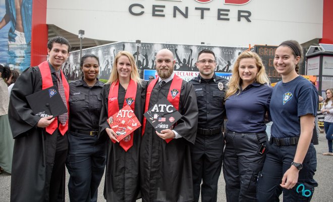 Group of students at commencement posing, some wearing EMS t-shirts.