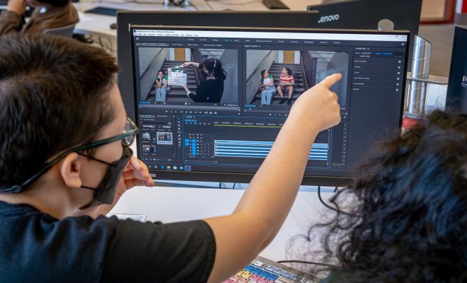 Student is pointing at a computer screen while video software is being displayed.