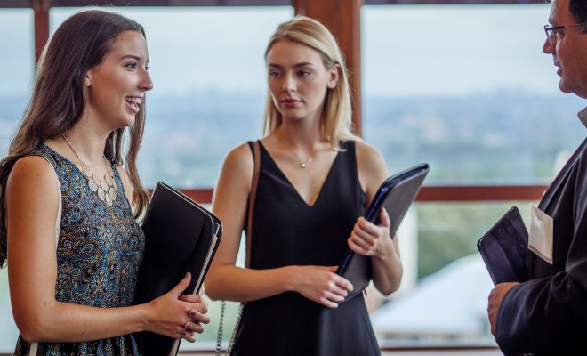 Two women are at a job fair with black notebooks in their hands.