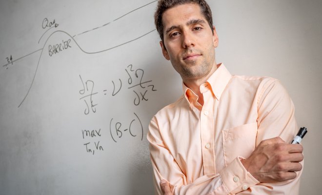 Jorge Trueba standing in front of a whiteboard with derivatives behind him, he has his arms crossed wearing a light button down.
