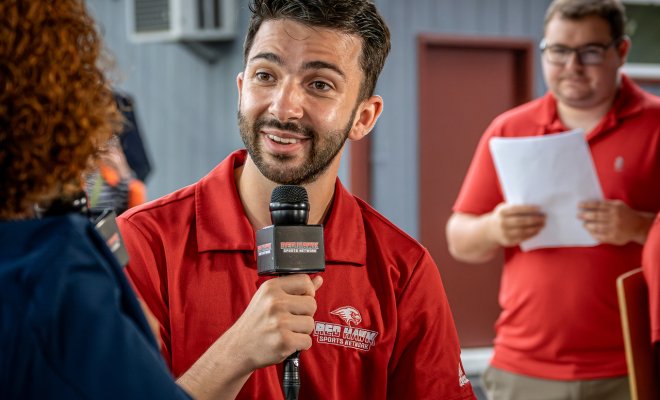 Man is holding a mic speaking with someone out of frame.