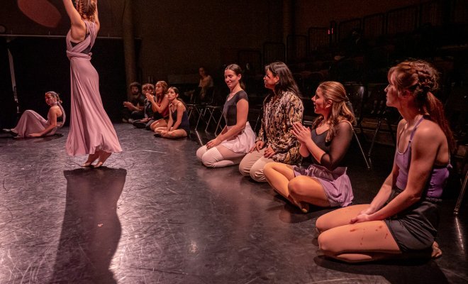 Students on stage sitting down watching someone perform.