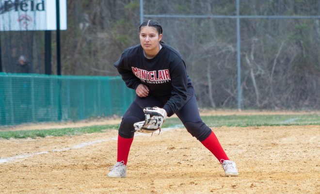 Female student playing softball with a Montclair State sweater on and a white baseball mitt.
