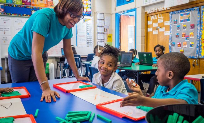 An Newark Urban Teacher Residency student helps elementary school children with math using counting blocks.