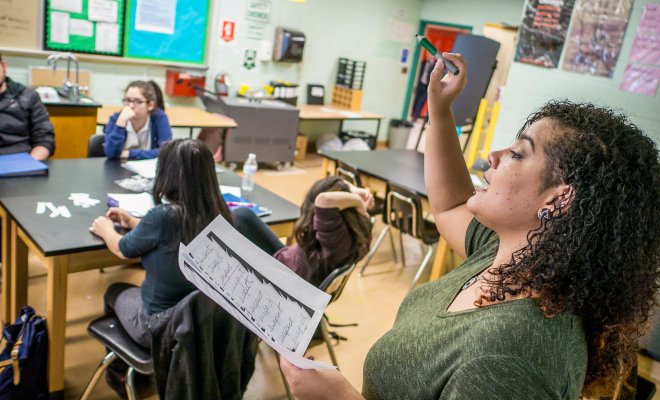 Teacher in a classroom full of students reading and giving a lesson.