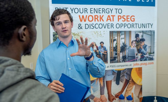Man in front of a PSEG sign, explaining something to someone else.