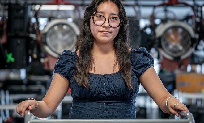 Pamela Hernandez stands in a campus broadcast media lab, surrounded by professional studio lights and equipment.