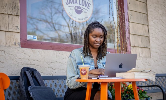Student wearing jean jacket seated with laptop outside a cafe