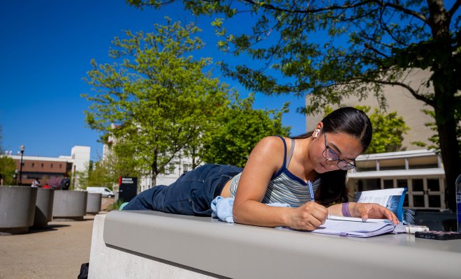 A student writes in a notebook outdoors.
