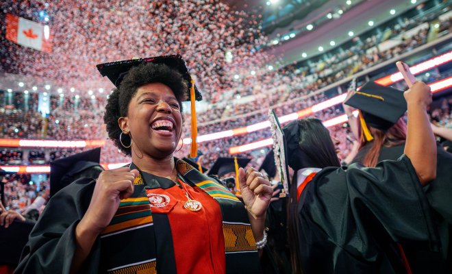 Graduate in cap and gown cheering as red and white confetti fills the air during Montclair State University’s 2026 Spring Commencement at Prudential Center.