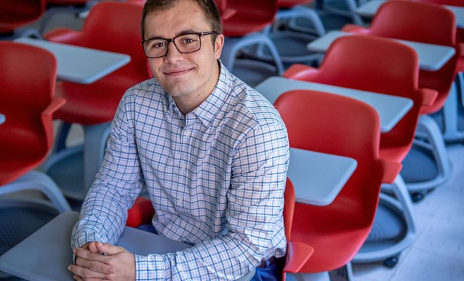 Jacob Roby sits in a classroom full of red chairs.