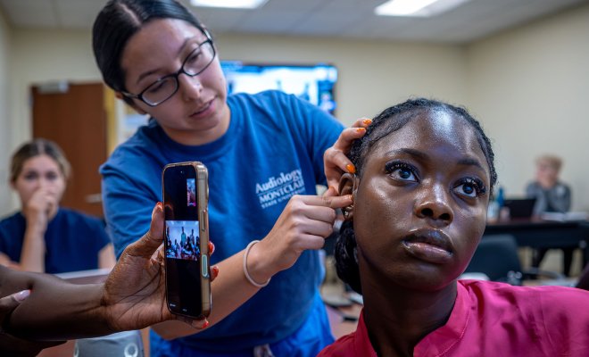 An audiology student fits another student with a hearing aid during a telehealth demonstration. 