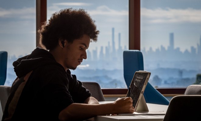 Student writing in front of windows with a view of the New York City skyline
