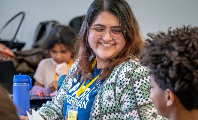 Female is smiling with glasses on smiling talking to a child.