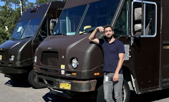 Man posing in front of two brown delivery trucks