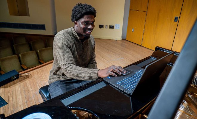 Student on stage at piano with computer.