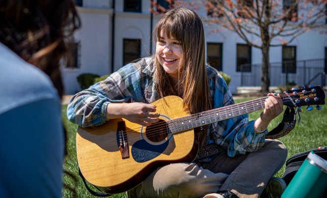 student playing the guitar while sitting in the grass