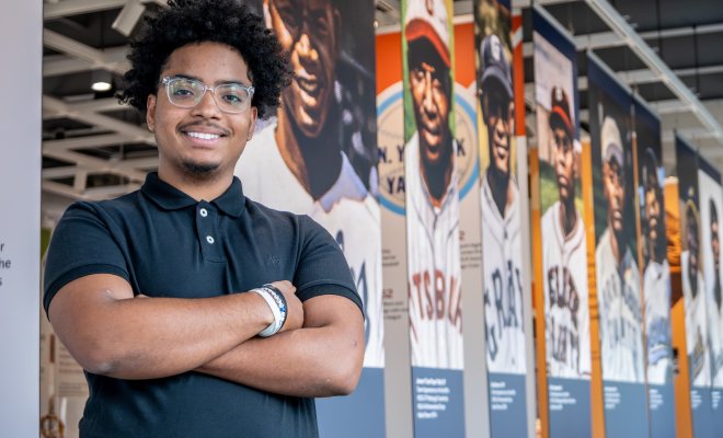 Edward Gonzalez stands with his arms crossed in front of famous ballplayers of the Negro Leagues.
