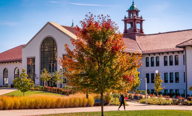 A student walks past Susan A. Cole Hall on Montclair State University’s campus as trees display colorful fall foliage.