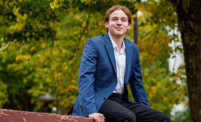 Ben Coulson sits on a wall on campus.