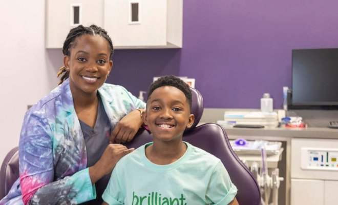 Pediatric patient sitting in dentist chair with Dr. Suffiyah Webb posing next to him 