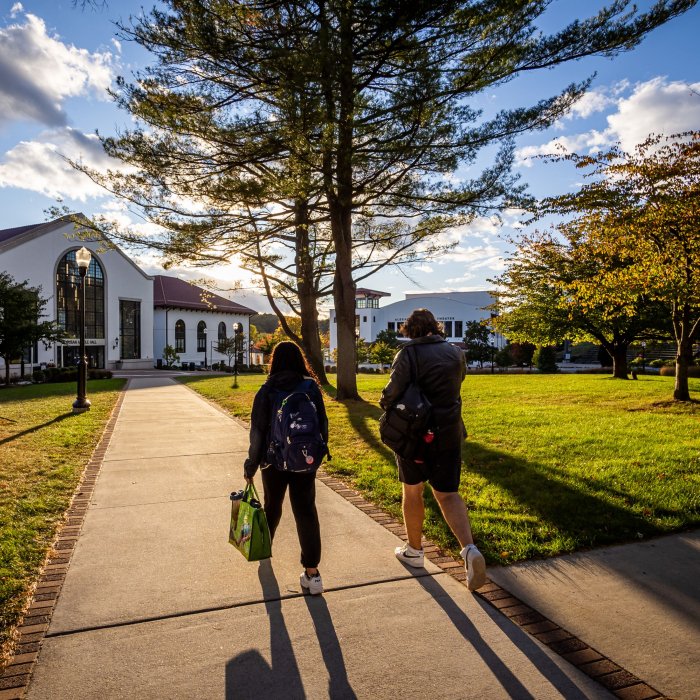 Two students walking toward Cole Hall as the sun sets behind it.