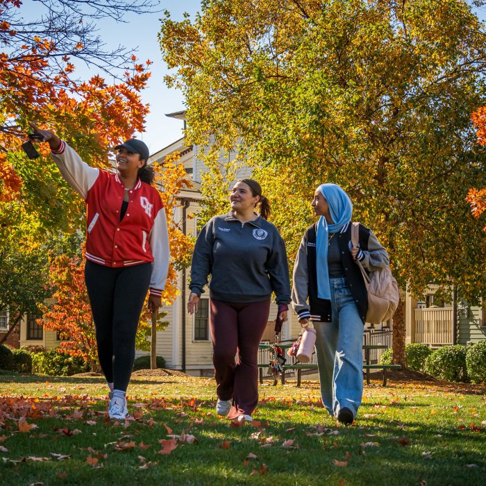 Three women students walk across the lawn under colorful fall foliage on the Bloomfield campus