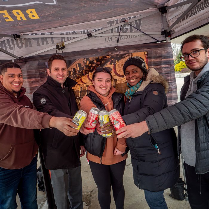 A group of five people in coats hold cans of beer.