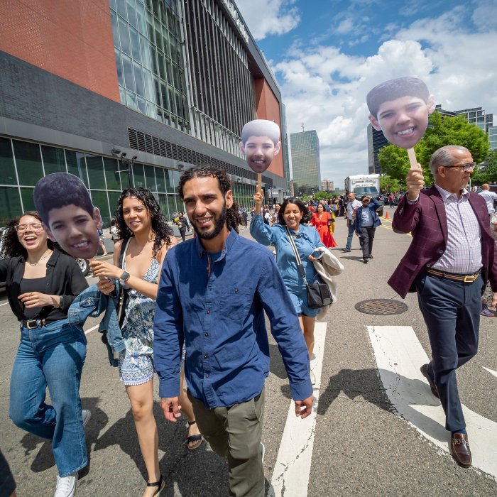 a graduate walking outside of prudential center flanked by family members holding up signs of their face.